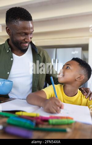 African american father and son sitting at table, writing in notebook smiling Stock Photo