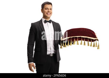 Elegant young man in a suit and bow tie holding a red velvet cushion isolated on white background Stock Photo