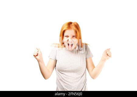 Beautiful young woman, natural redhead with clenched fists up & scary angry facial expression. Attractive female with red hair, screaming, unleashing Stock Photo