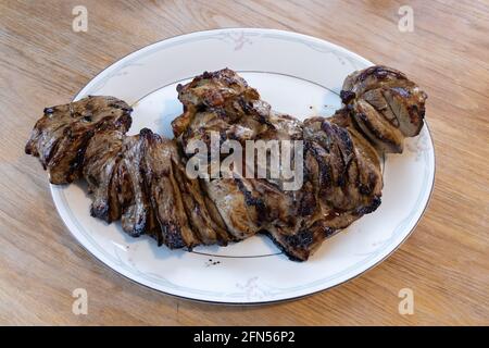 Butterflied leg of lamb, cooked on a barbecue and served on a bone china serving dish, Suffolk UK Stock Photo