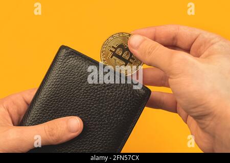 Man puts bitcoin in his leather wallet, pay with cryptocurrency concept background Stock Photo