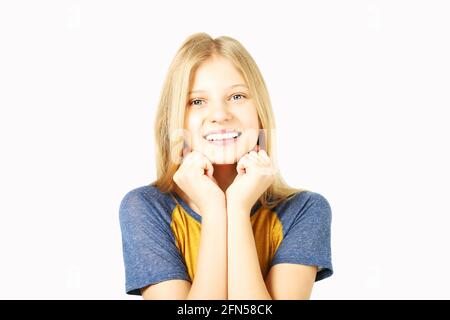 Young beautiful teenage girl with golden blond hair in wearing yellow baseball t-shirt with blue sleeves. Pretty female smiling, hands on chin, standi Stock Photo