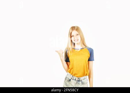 Young beautiful teenage girl with blond hair wearing yellow baseball t-shirt with blue sleeves, pointing at copy space with her finger. Pretty girl sm Stock Photo