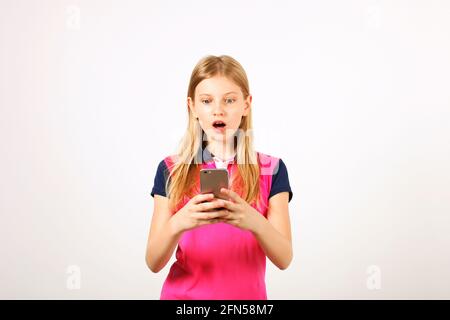 Young amazed woman wearing yellow blue baseball shirt receiving surprising text message on cell phone with open mouth. Astonished blonde teenage femal