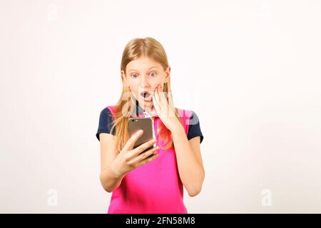 Young amazed woman wearing yellow blue baseball shirt receiving surprising text message on cell phone with open mouth. Astonished blonde teenage femal Stock Photo