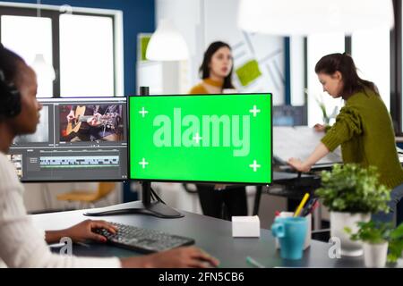 Black woman videographer employee with headphones using computer with green screen, chroma key mockup isolated display sitting in video production studio. African editor processing film montage Stock Photo