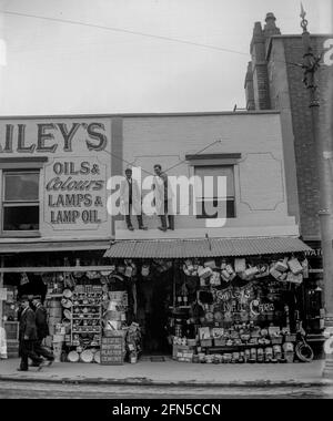 Two men work on the canopy of Bailey's Stores in Gloucester Road, Bristol around 1910. A hardware store with its stock very much on display on from the street in the days when lamp oil was important to everyone. Stock Photo