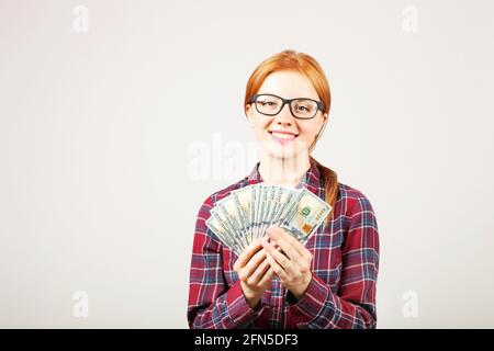 Portrait of young beautiful redhead woman with fistful of money holding one hundred dollar bill stack like fan. Excited attractive red hair female w/ Stock Photo