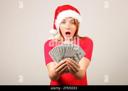 Money as a Christmas present concept. Portrait of happy young redheaded woman holding bunch of one hundred dollar bills received as new years gift. Gr Stock Photo