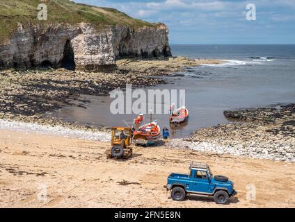 Flamborough, East Yorkshire, UK, 12th May 2021 - Two small fishing boats approaching the shore to land catch being hauled on to beach by a yellow trac Stock Photo