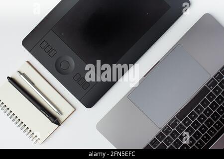 Top view photo of a, notepad, pen, black graphic design tablet, stylus and a laptop on a white background. Stock Photo