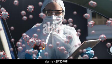 Composition of covid 19 cells floating over doctor in ppe suit and face mask measuring temperature Stock Photo