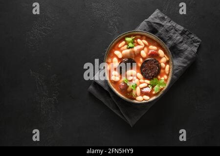 Spanish fabada with chorizo, morcilla, sausage, haricot on black background with copy space. Top view. Asturian hearty bean stew. Stock Photo