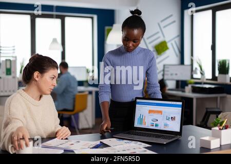 Diverse businesswomen discussing new project for company evolution, black woman checking tasks on new contract. Multiethnic employees gathered in co-working space. Stock Photo