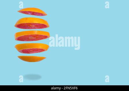 Floating levitating ripe grapefruit on blue background. Vitamins, healthy diet concept. Minimal fruit idea. Sliced grapefruit floating in the air. Cre Stock Photo