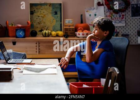 A focused boy with knees inside shirt sits at computer at home Stock Photo
