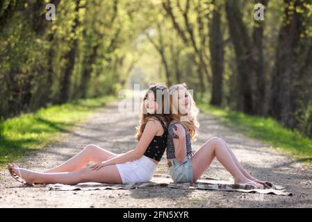 Two pretty teen girls sitting on a tree lined country road. Stock Photo