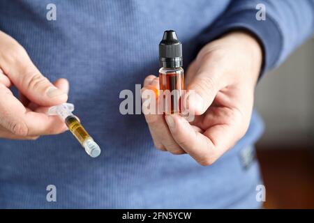 hands holding a syringe of co2 oil and a bottle of cannabis distillate Stock Photo