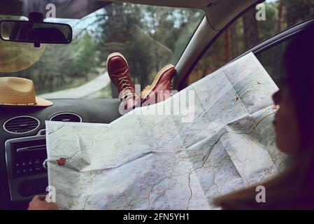 Woman sitting in her car looking at a map. She is in a forest. Stock Photo