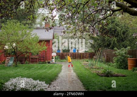 A little girl plays in the pouring rain in backyard garden Stock Photo
