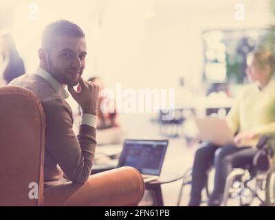 businessman using laptop at office disabled woman in wheelchair in background Stock Photo