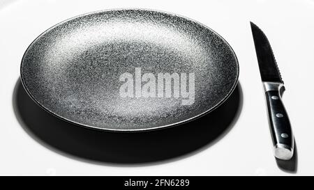 Black dessert plate and steel knife on white background Stock Photo