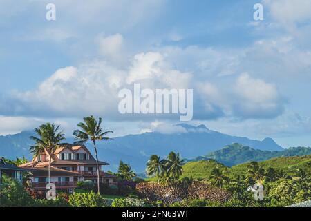 House sits on hill surrounded by palm trees on tropical island against mountains Stock Photo