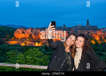 Women taking selfie with Pitigliano medieval city in the back at sunset. Stock Photo
