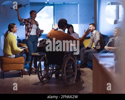Disabled businessman in a wheelchair at work in modern open space coworking office with team using virtual reality googles drone assistance simulation Stock Photo