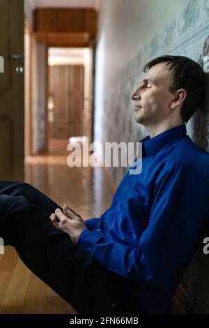 A young tired man is sitting on the floor in the corridor. Blue light. Stock Photo