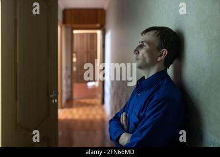 A young tired man is sitting on the floor in the corridor. Blue light. Stock Photo