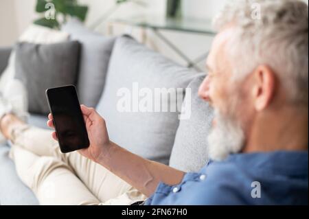 Middle-aged man holding smartphone with black empty screen, back view, blank screen for advertising app, copy space. Mockup concept Stock Photo