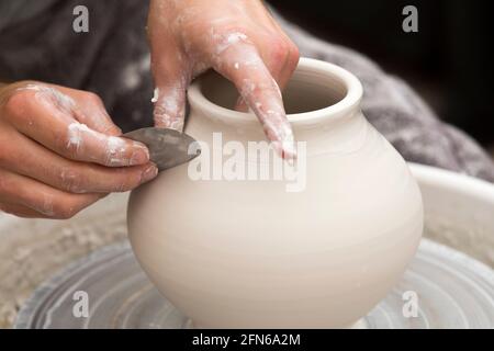 Potter / potters hands using a metal turning tool skilfully hand throwing a ceramic thrown clay vase pot on a turning wheel. England. UK (123) Stock Photo