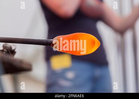 A glass blower's pipe with a gob (or blob) of molten glass on the end, resting, rotating, rolling & shaping the glass, working it on the flat metal 'Marver' ready to be blown by the glass blower. UK (123) Stock Photo