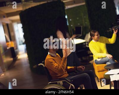 Disabled businessman in a wheelchair at work in modern open space coworking office with team using virtual reality googles drone assistance simulation Stock Photo