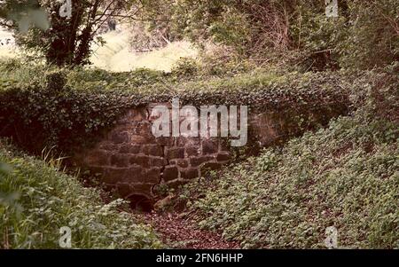 A simple bridge construction: a pipe with bricks placed over it. The stream is dry at the moment. The brickwork shows cracks. It looks old and rustic Stock Photo