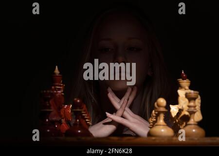the girl looks thoughtfully at the chessboard against a dark background. old chess. business concept Stock Photo