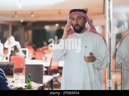 Middle eastern Arab businessman in the office speaking on smartphone in front of his team  Stock Photo