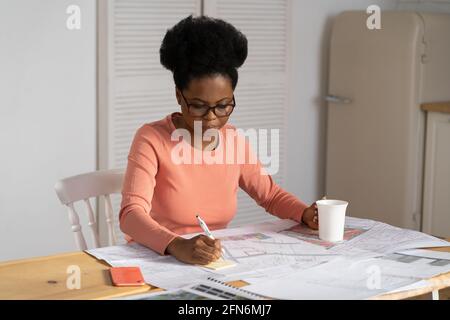 Concentrated architect woman draw blueprint work at home. Black female designer create project plan Stock Photo