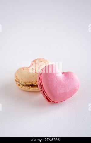 Two heart-shaped French macaron cookies, vanilla and strawberry flavour, copy space on neutral background, vertical Stock Photo