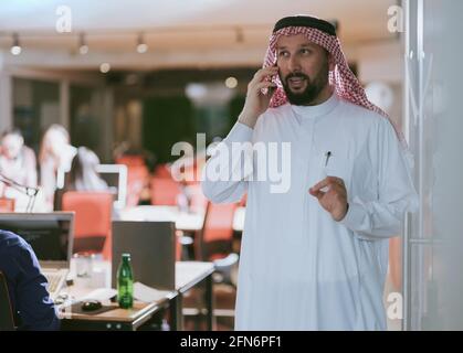 Middle eastern Arab businessman in the office speaking on smartphone in front of his team  Stock Photo