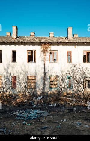 The facade of an abandoned two-story house with broken glass and boarded-up windows Stock Photo