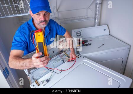 An appliance technician testing circuits on a residential washing machine, in uniform, looking at the volt meter Stock Photo
