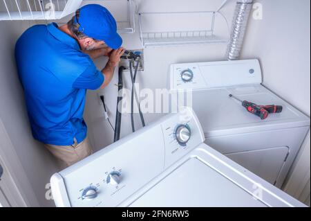 Plumber installing a residential washing machine, hooking up the water supply line Stock Photo