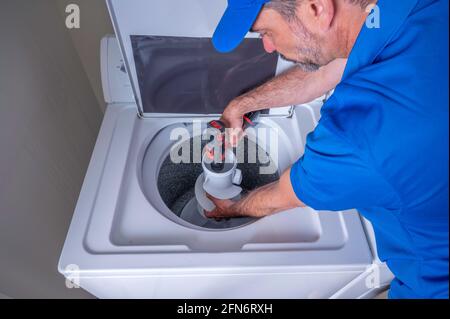 Appliance technician in a blue uniform installing a agitator on a washing machine, using a cordless drill Stock Photo