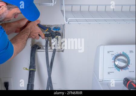 Plumber in a residential home hooking up water supply lines for a washing machine, appliance repair service Stock Photo