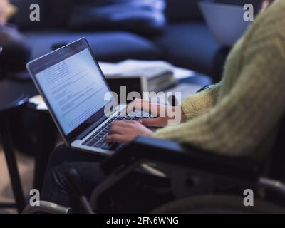 Young woman in wheelchair working on laptop at office. Getting an education at home concept Stock Photo