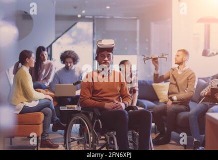 Disabled businessman in a wheelchair at work in modern open space coworking office with team using virtual reality googles drone assistance simulation Stock Photo