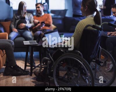 Young woman in wheelchair working on laptop at office. Getting an education at home concept Stock Photo