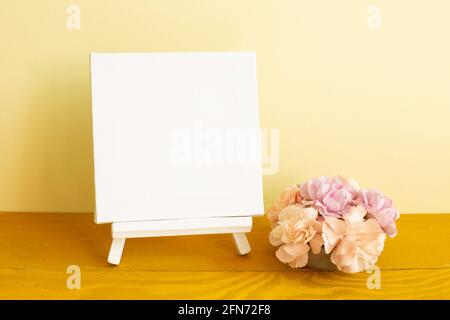 Blank white canvas with carnation flowers on wooden table. yellow background Stock Photo